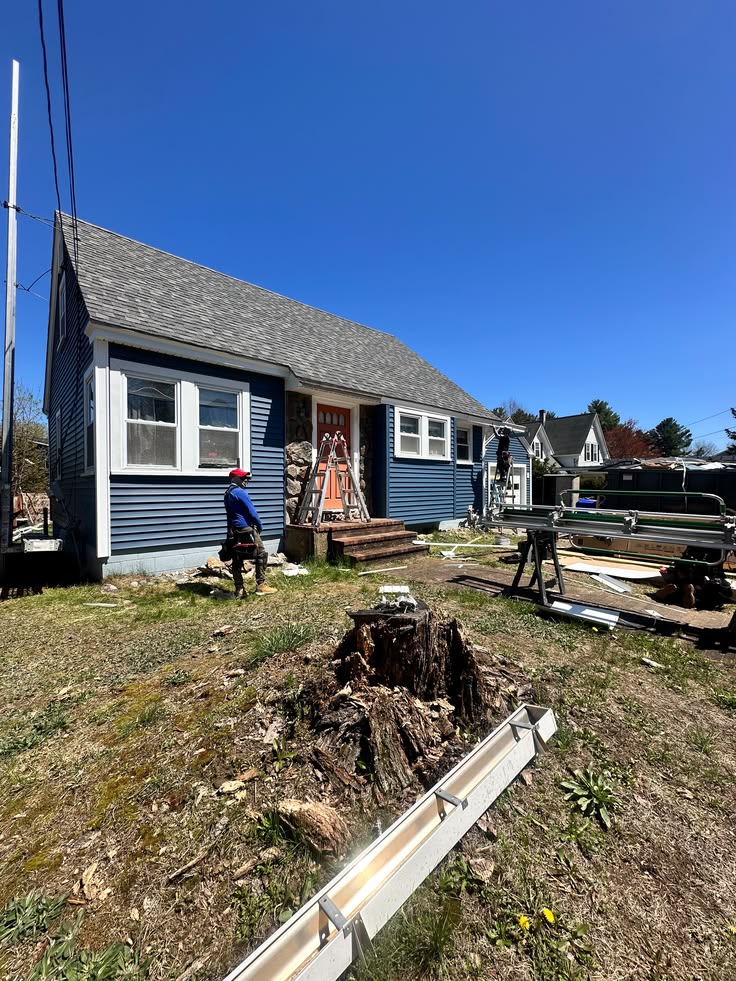 Exterior repair work on blue-sided home with ladder and materials on site