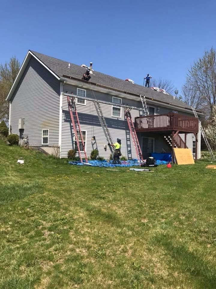 Crew replacing roof and siding on two-story home with ladders staged